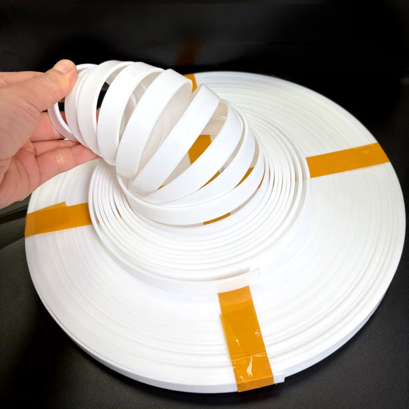 A hand lifting loops of white PTFE guide strip from a coil